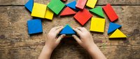 Child hands assembling colorful wooden geometric shapes on rustic wood table. Educational toy blocks for learning and development activities.