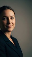 Professional young businesswoman in dark suit smiling confidently against neutral background for corporate marketing and business communications.