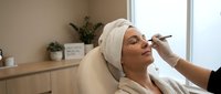 Young woman receiving professional eyebrow shaping treatment at modern beauty salon. Relaxing spa facial care procedure with expert beautician application.