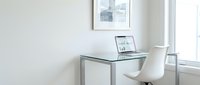Modern minimalist home office workspace with glass desk, white chair and laptop displaying charts for remote work productivity and business analysis.