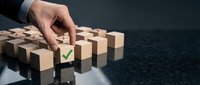 Businessman hand selecting wooden cube with green checkmark from group of blocks on dark surface for decision making and quality control concepts.