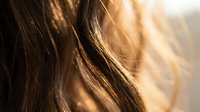 Flowing brown hair with golden sunlight creating warm highlights and natural movement in soft focus artistic portrait photography.