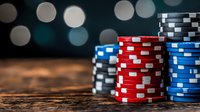 Stacks of poker chips in red, blue and black on rustic wooden table with blurred bokeh lights background creating atmospheric casino ambiance.