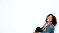 Young woman with curly dark hair and medium skin tone wearing denim jacket and patterned scarf, looking upward thoughtfully against white background for portrait and lifestyle use.