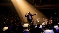 Orchestra conductor leading symphony performance in dramatic spotlight before packed concert hall audience creating inspiring musical atmosphere.