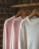 Soft pink and white sweaters hanging on wooden hangers against rustic brick wall background, minimalist fashion composition for retail and style blogs.