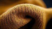 Close-up macro shot of beige knitted wool fabric texture showing detailed stitch pattern and fiber structure in warm golden lighting, suitable for textile design backgrounds.