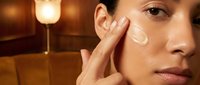 Young woman applying facial cream moisturizer in warm bathroom lighting. Skincare routine, beauty treatment, self-care concept for cosmetic advertising.