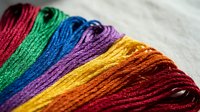 Colorful embroidery thread skeins arranged in rainbow spectrum on white fabric background for needlework and crafting projects.