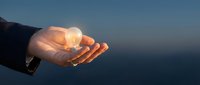 Business professional holding glowing light bulb in cupped hands against blue sky background symbolizing innovation creativity and bright ideas for success.