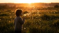 Young child standing in wildflower meadow at golden hour sunset, holding flowers, backlit by warm sunlight with sparkling bokeh effect for nature and childhood themes.