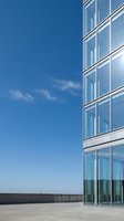 Modern glass and steel office building facade with reflective windows against clear blue sky and concrete plaza, suitable for corporate, business, and architectural design projects.