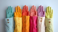 Colorful rubber gloves with decorative fabric cuffs featuring wooden buttons arranged in a row against white background, showcasing vibrant household cleaning accessories.
