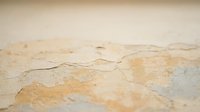 Cracked and peeling paint on aged wall surface showing weathered texture with beige and tan tones, suitable for backgrounds and design projects.