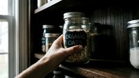 Hand holding glass jar labeled organic oats on wooden shelf with storage containers, pantry organization and healthy food storage for kitchen design and lifestyle content.