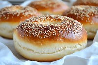 Fresh baked sesame seed hamburger buns with golden brown crust on white paper, ready for grilling and barbecue meals.