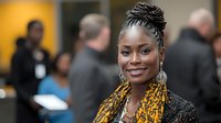 Young African American businesswoman with braided updo hairstyle and traditional print dress smiling confidently at professional networking event, corporate diversity.