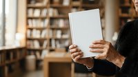 Man holding blank white tablet in library with bookshelves in background, suitable for mockups, education, technology, and business presentations.