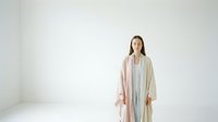 Woman with long dark hair, East Asian ethnicity, wearing a light gray dress with a beige cardigan, standing against a white background in a minimalist studio setting.