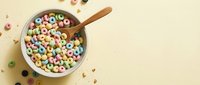 Colorful breakfast cereal rings in white bowl with wooden spoon on beige background. Sweet morning meal with milk for kids and adults nutrition concept.