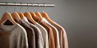Neutral beige and brown sweaters hanging on wooden hangers in organized closet wardrobe for seasonal fashion storage and minimalist home organization.
