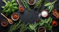 Fresh herbs and spices arranged on dark slate background with wooden bowls and utensils creating culinary frame for cooking and seasoning recipes.