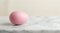 Single pink egg on marble surface with neutral beige background for Easter holiday decoration and spring seasonal design concepts.