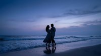 Romantic couple silhouettes dancing on beach at twilight with purple sky and ocean waves. Love, romance and relationship concept for wedding invitations.
