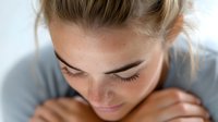 Young woman with closed eyes and gentle smile in peaceful contemplative moment, head bowed, wearing casual grey top, expressing serenity and mindfulness.