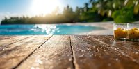 Rustic wooden deck overlooking tropical beach at sunset with refreshing iced drinks, palm trees and turquoise ocean water creating serene vacation atmosphere.