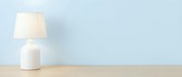 Minimalist white ceramic table lamp with linen shade on wooden surface against soft blue wall for home decor and interior design.