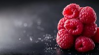 Fresh red raspberries stacked on dark surface with water droplets and bokeh lighting effects for culinary and healthy eating concepts.