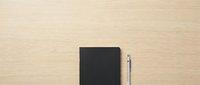 Black notebook and pen on wooden desk surface, flat lay composition for business, education, and office design projects.