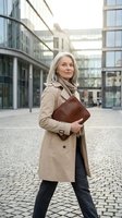 Confident mature businesswoman with silver hair walking in modern office district holding leather portfolio, professional corporate lifestyle.