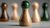 Wooden game piece with green top standing out among blurred pawns on neutral background for board games and strategic thinking concepts.