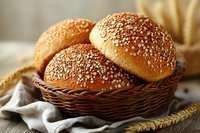 Fresh homemade sesame burger buns in rustic wicker basket on wooden table with wheat ears and linen napkin, golden brown crusty bread rolls for sandwiches.