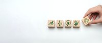 Hand placing wooden cube with recycling symbol completing row of eco-friendly icons on white background for sustainable business concepts.