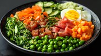 Fresh poke bowl with raw tuna, green peas, boiled egg, cucumber, carrots and seaweed on black plate, healthy food composition for restaurant menu.