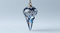 Crystal glass ornament with faceted teardrop design hanging from gold string, featuring blue accents and light reflections against neutral background.