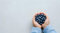 Overhead view of hands holding fresh blueberries on neutral background, suitable for food, health, nutrition, and wellness marketing materials.