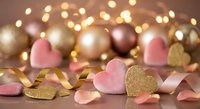 Romantic Valentine's Day decoration with pink and gold heart shapes, ribbon, ornaments and warm bokeh lights for love celebration.