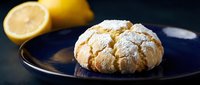 Lemon crinkle cookie with powdered sugar on dark plate, fresh citrus fruit in background, homemade baked dessert for cafes and bakeries.