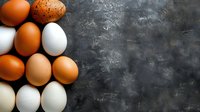 Fresh farm eggs in various natural shades from white to brown arranged on dark rustic concrete background with copy space. Food photography layout.