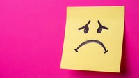 Yellow sticky note with sad face drawn in black marker on bright pink background expressing negative emotions and feelings.
