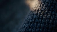 Close-up macro shot of dark blue knitted wool fabric texture with soft focus background, showcasing intricate fiber details and cozy winter material patterns.