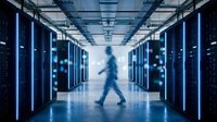 Blurred silhouette of person walking through modern data center corridor with blue server racks and bright lighting for technology concepts.