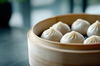 Steamed dumplings in traditional bamboo basket on dark surface, selective focus on white pleated dim sum showing delicate folds and texture.