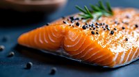 Fresh raw salmon fillet with black pepper and rosemary herb on dark background, close up view. Gourmet seafood cooking ingredient for healthy meal.