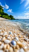 Gentle waves wash over smooth pebbles on tropical beach shore with turquoise water, lush green vegetation and bright blue sky with wispy clouds.