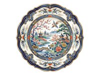 Ornate porcelain plate with scalloped edges featuring traditional Asian landscape design, pagoda, flowering trees, birds, and water elements in blue, green, and coral tones on cream background.